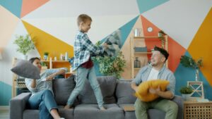 Porodica na sivom kauču u dnevnoj sobi igra se jastucima.