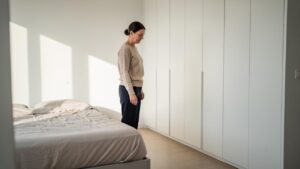Žena stoji u minimalnoj spavaćoj sobi pored belog ormara