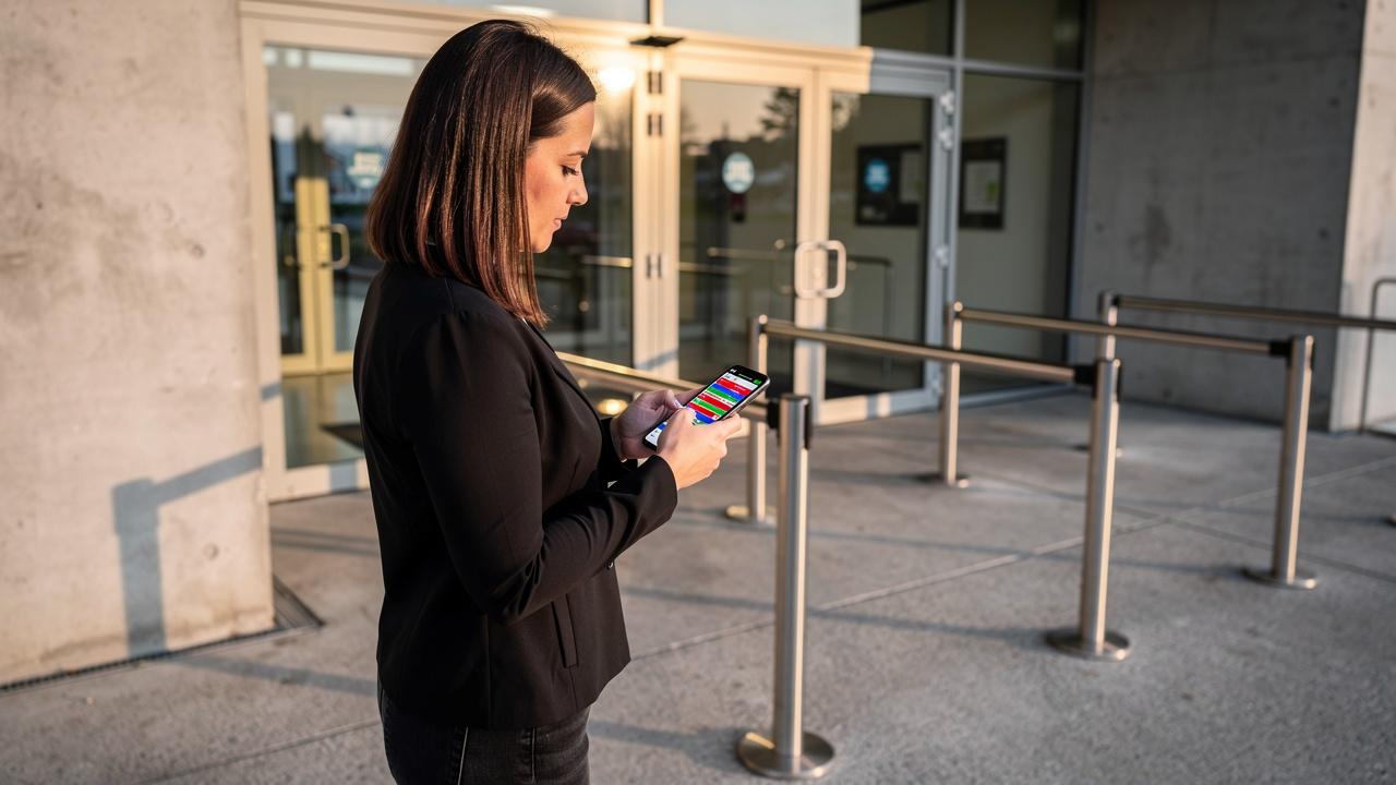 Žena stoji ispred ulaza u zgradu i koristi mobilni telefon