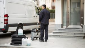 Radnik stoji pored kolica i opreme za čišćenje ispred ulaza zgrade